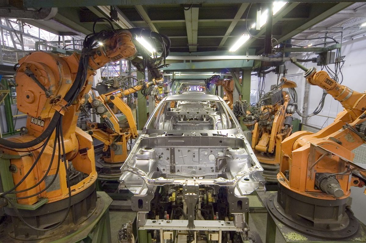 Rows of industrial robot arms working on a car body